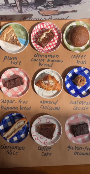 Nine hand-painted Dugdugi plates in checks and florals, each holding a bakery treat with a handwritten label