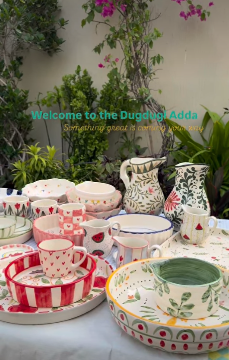 Hand-painted Dugdugi mugs, jugs, bowls and platters arranged on a garden table at the Dugdugi Adda