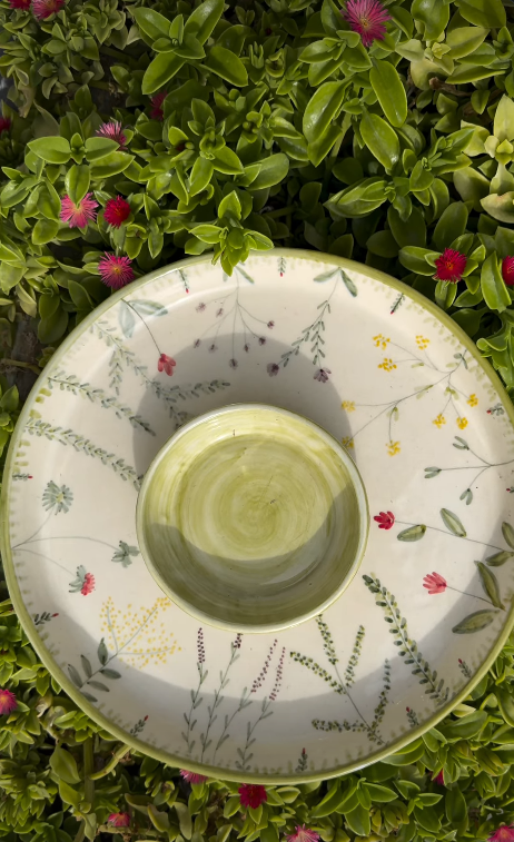Chip and dip platter with a green centre bowl and delicate wildflower painting, resting on garden plants