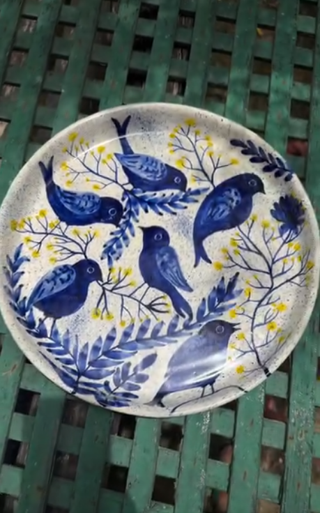 Speckled platter hand-painted with blue birds and yellow blossoms on a green bench